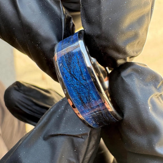 Close-up of a pet memorial blue ring held by black gloves showing pet hair and colored inlay against a blurred background