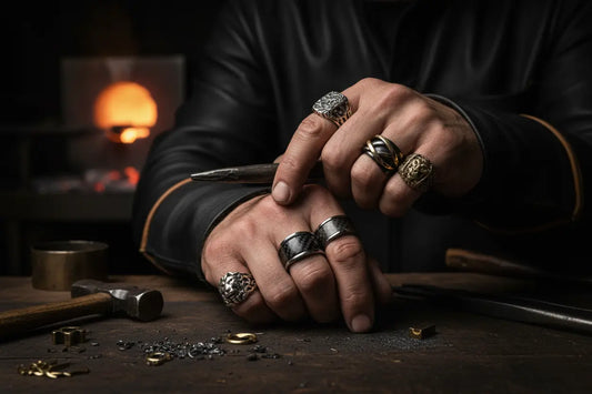 Artisan jeweler's masculine hands wearing handcrafted rings on different fingers in forge workshop - premium custom jewelry including glow rings, tungsten bands, and carbon fiber rings displayed over workbench with forge tools and warm ember lighting